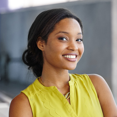 A smiling young woman with dark hair, wearing a yellow top and a lanyard, posing against a blurred background.