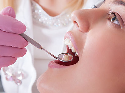 Woman receiving dental care with a dentist using a drill on her teeth.