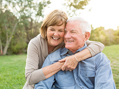 The image shows an elderly couple embracing each other outdoors during daylight.